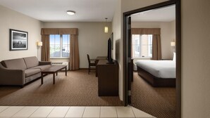 Una habitación de hotel con cama, sofá, escritorio, televisor y ventana con cortinas.