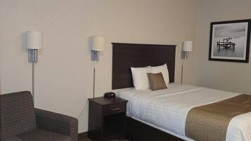 A hotel room with a bed, a chair, a nightstand, and two wall-mounted lamps.