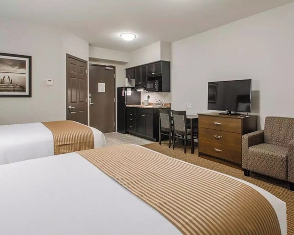 Una habitación de hotel con dos camas, un kitchenette, un televisor y un sofá.