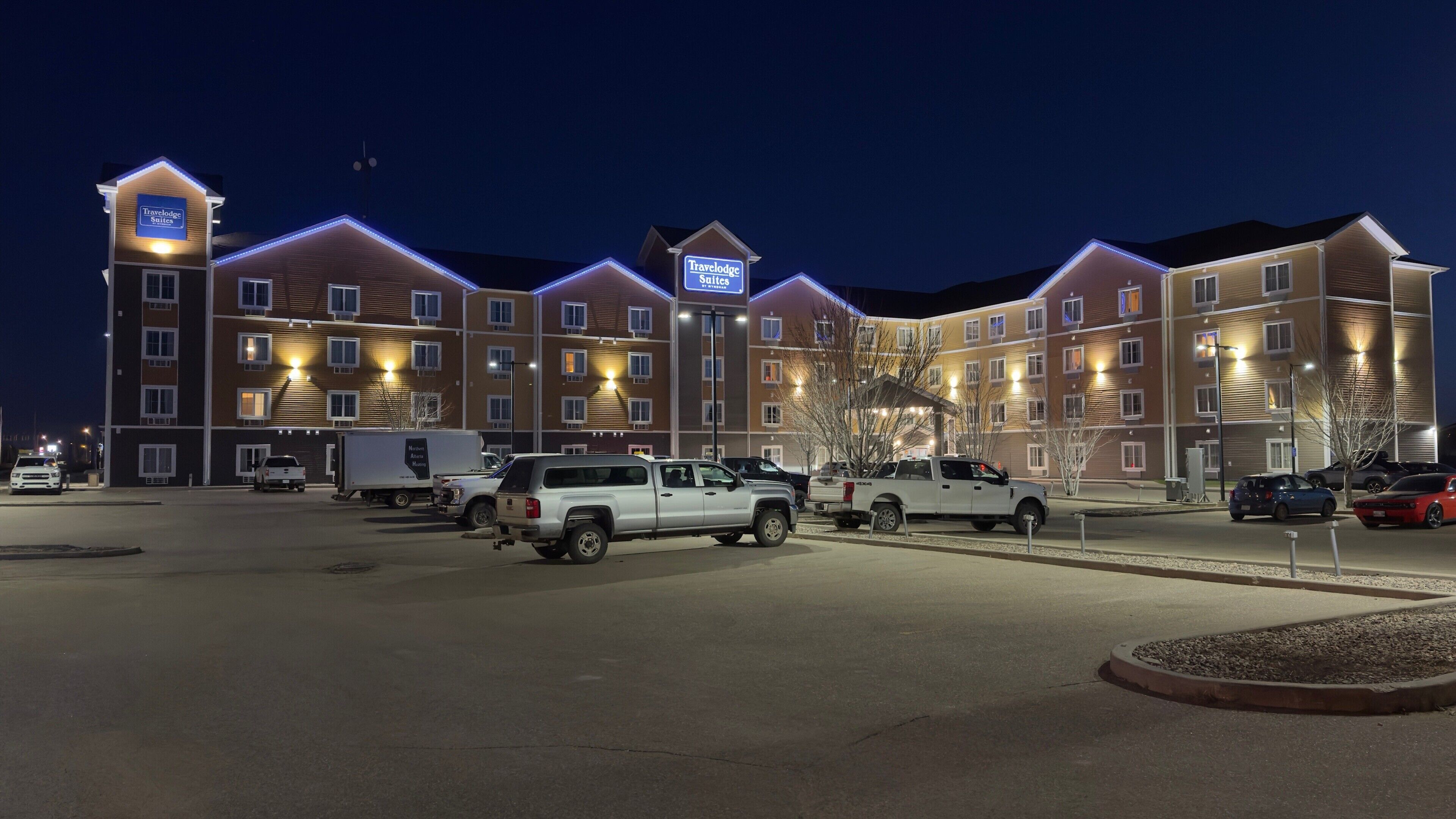 A multi-story hotel with illuminated signage, a parking lot with several vehicles, and a well-lit exterior.