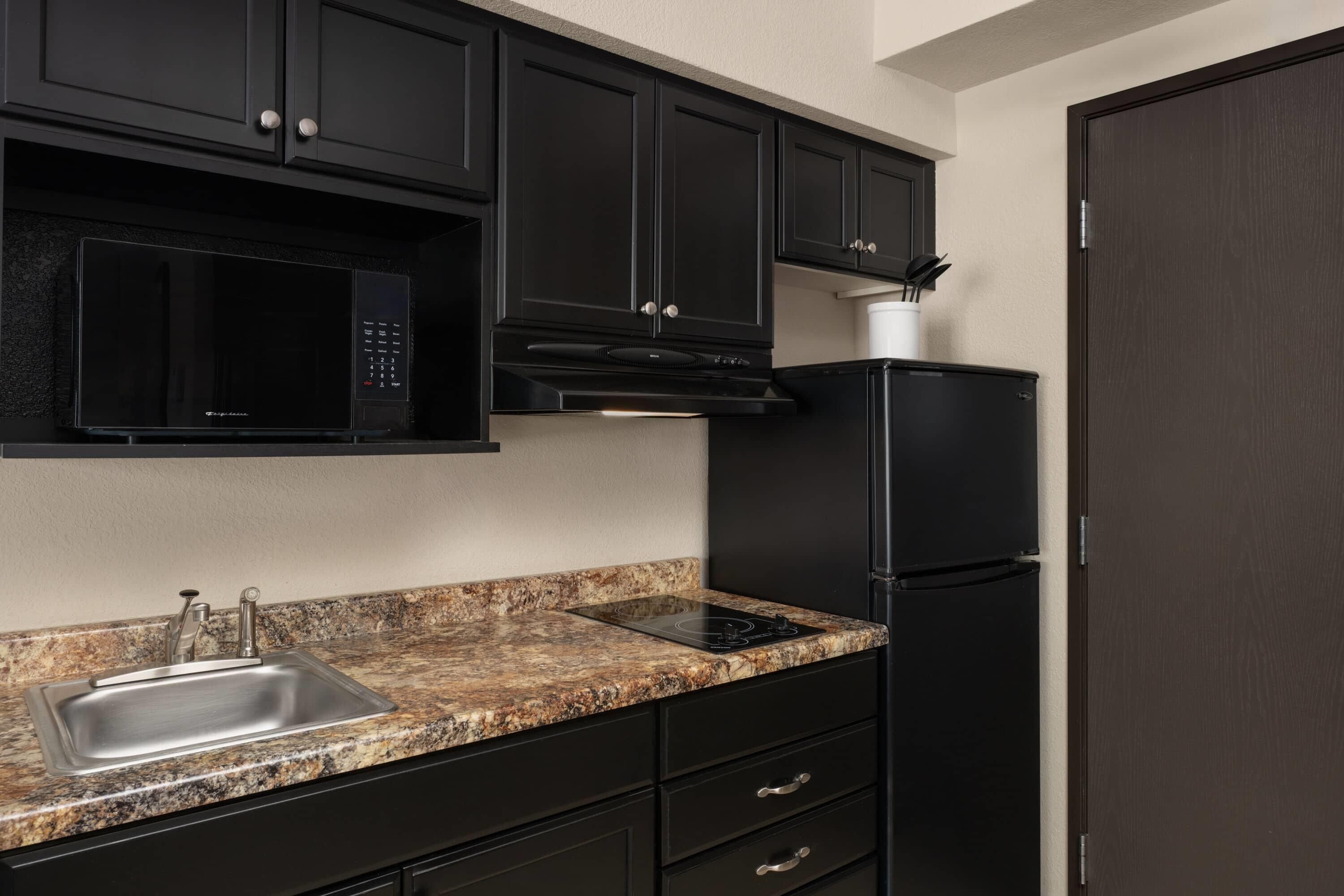 A kitchen with black cabinets, a stainless steel sink, a microwave, an induction cooktop, and a refrigerator.