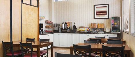 Comedor de hotel con mesas y sillas de madera, una cocina al fondo y un cuadro en la pared.