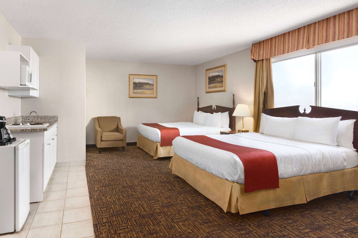 A hotel room with two beds, a desk with a refrigerator, and a chair.