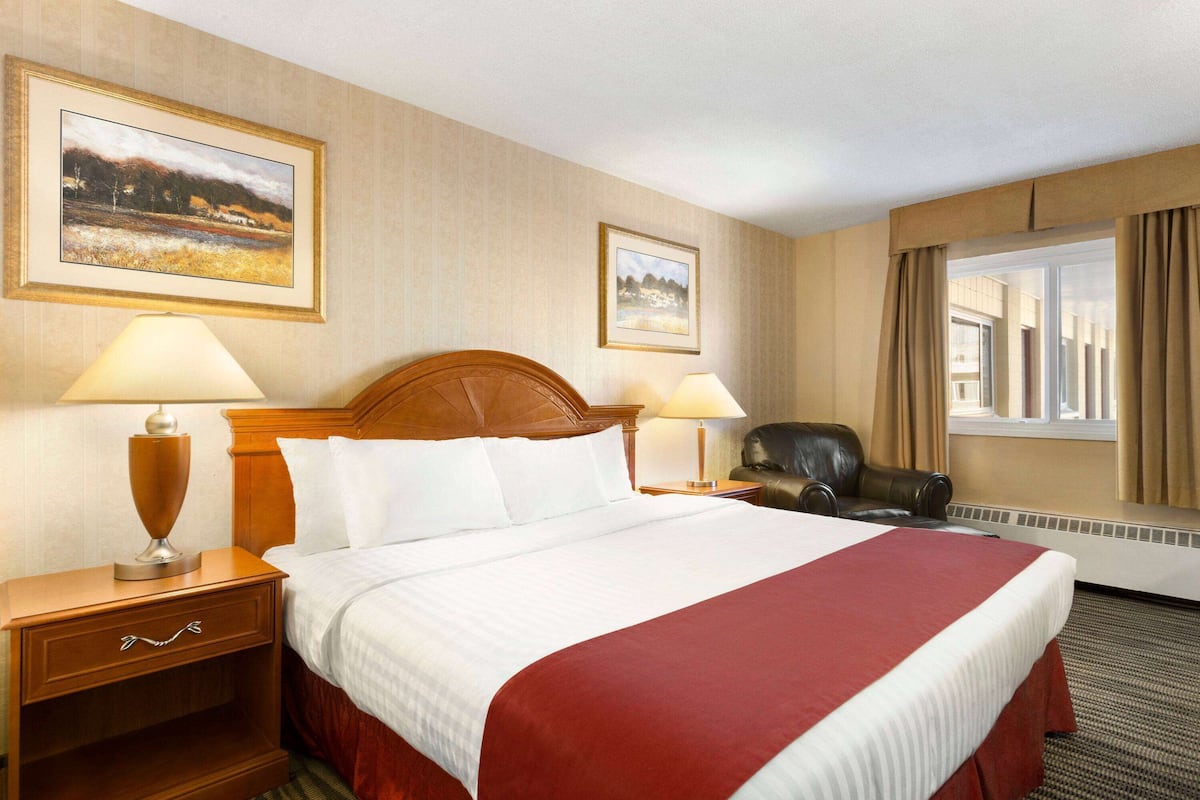 A hotel room with a large bed, two bedside tables with lamps, a chair, and two framed pictures on the wall.