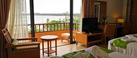 A hotel room with a balcony, a TV, a desk, and two beds.