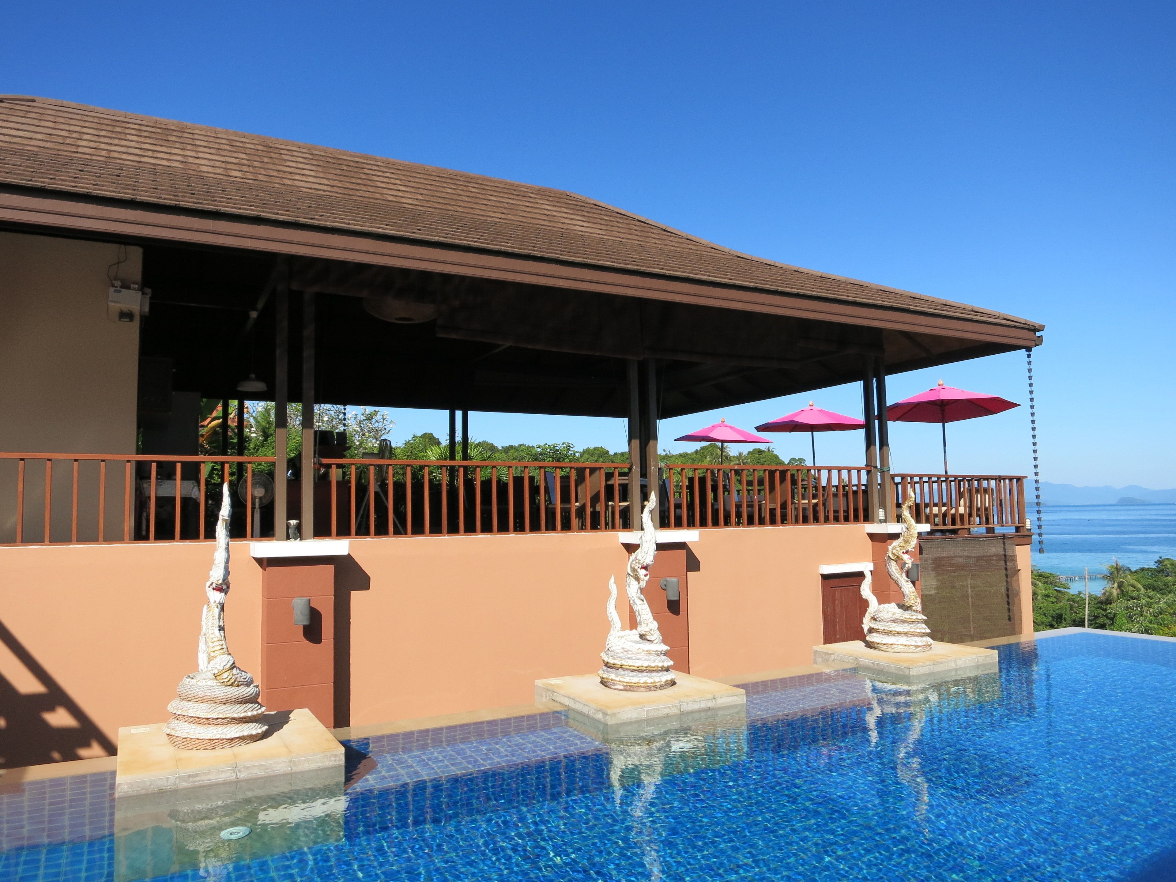 A swimming pool with clear blue water, a covered deck area with a railing, and a view of the ocean.