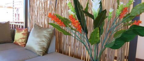 A room with a beige sofa, a woven bamboo partition, and a potted plant with green leaves and orange flowers.