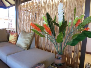 A room with a beige sofa, a woven bamboo partition, and a potted plant with green leaves and orange flowers.