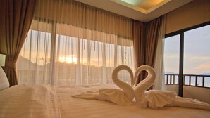 Ein Hotelzimmer mit Bett, durchsichtigen Vorhängen und Blick auf den Sonnenuntergang durch das Fenster.