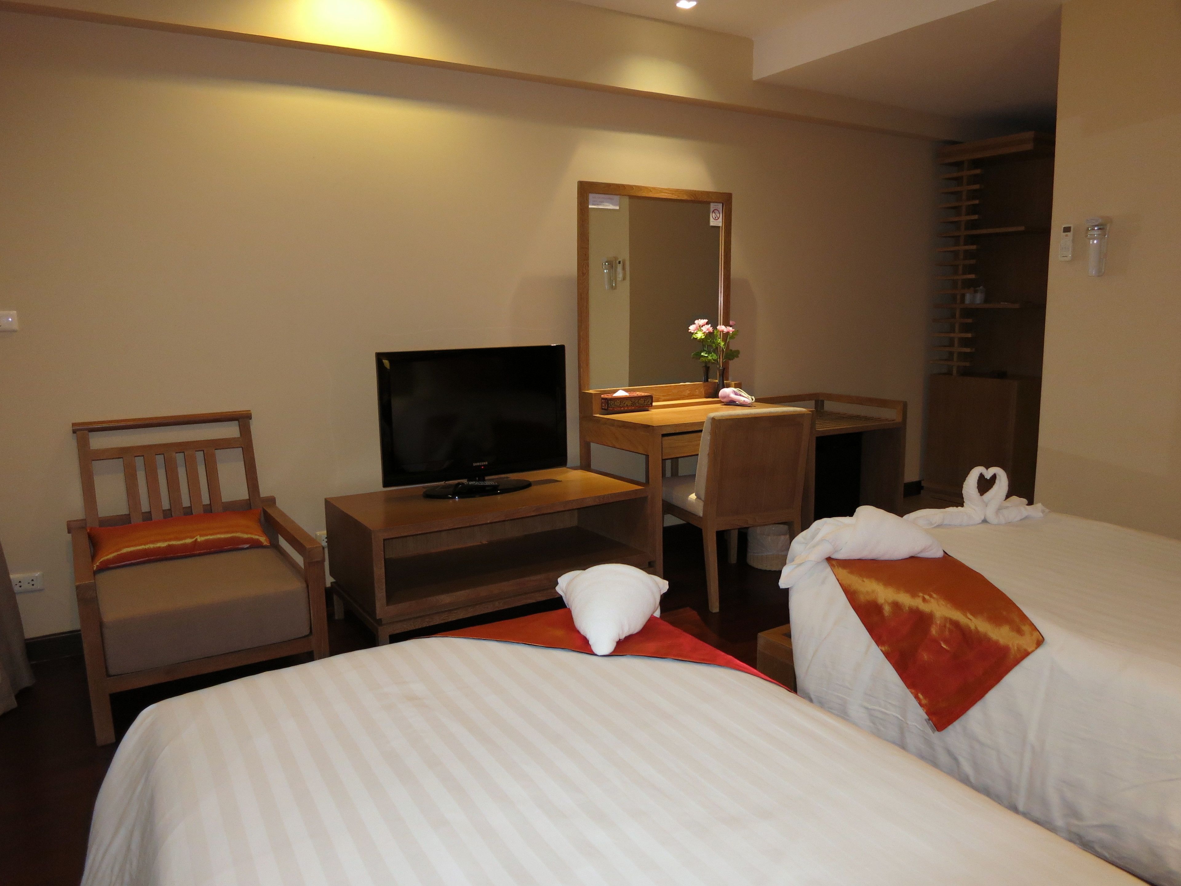 A hotel room with two beds, a TV, a desk, a chair, a mirror, and a shower area.