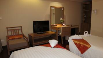A hotel room with two beds, a TV, a desk, a chair, a mirror, and a shower area.