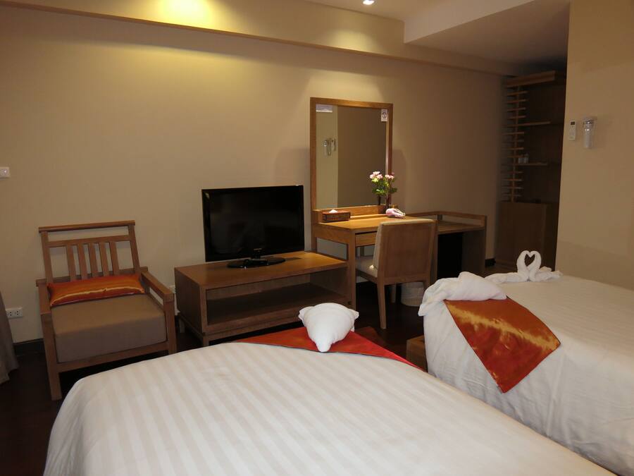 A hotel room with two beds, a TV, a desk, a chair, a mirror, and a shower area.