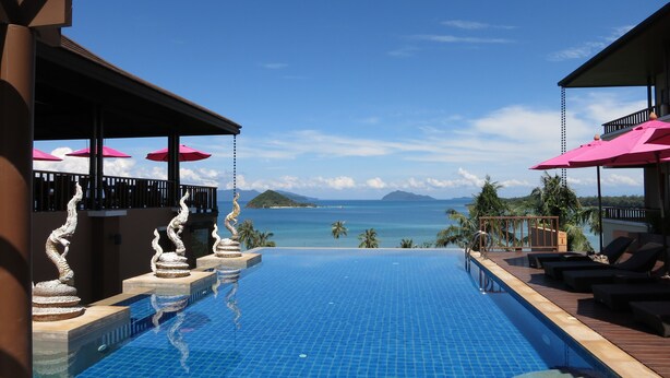 Ein Infinity-Pool mit Blick auf das Meer und die Berge, umgeben von Liegestühlen und Sonnenschirmen.