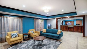 Un hall de hotel con mostrador de recepción, un sofá azul, un sillón amarillo y una pequeña mesa redonda.