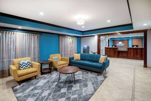 Un hall de hotel con mostrador de recepción, un sofá azul, un sillón amarillo y una pequeña mesa redonda.
