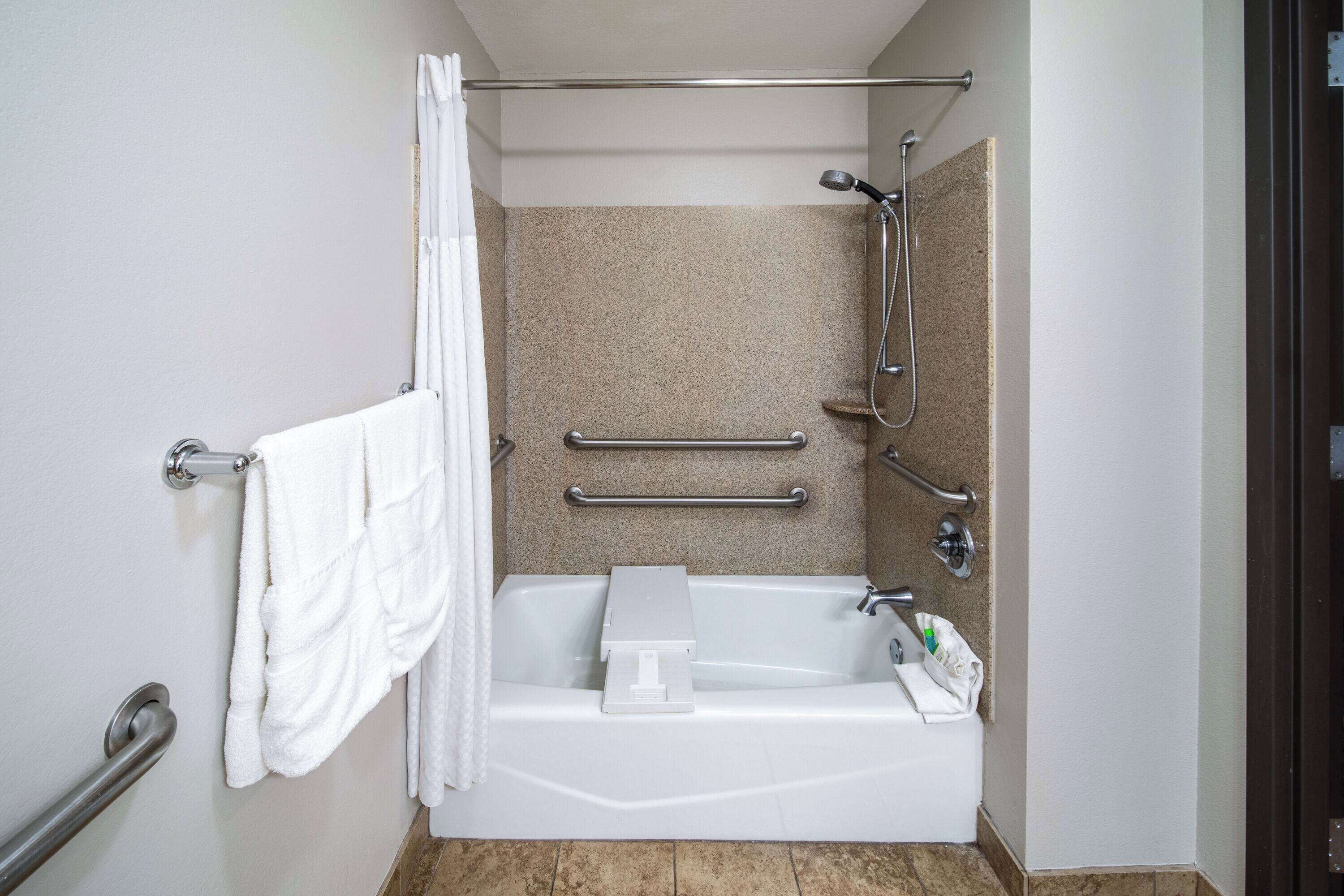 A bathroom with a bathtub, shower, and grab bars.