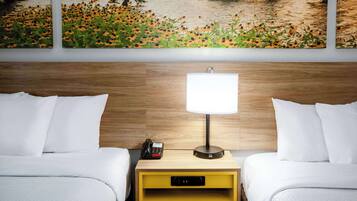 A hotel room with two beds, a nightstand with a lamp, a phone, and a small yellow drawer.