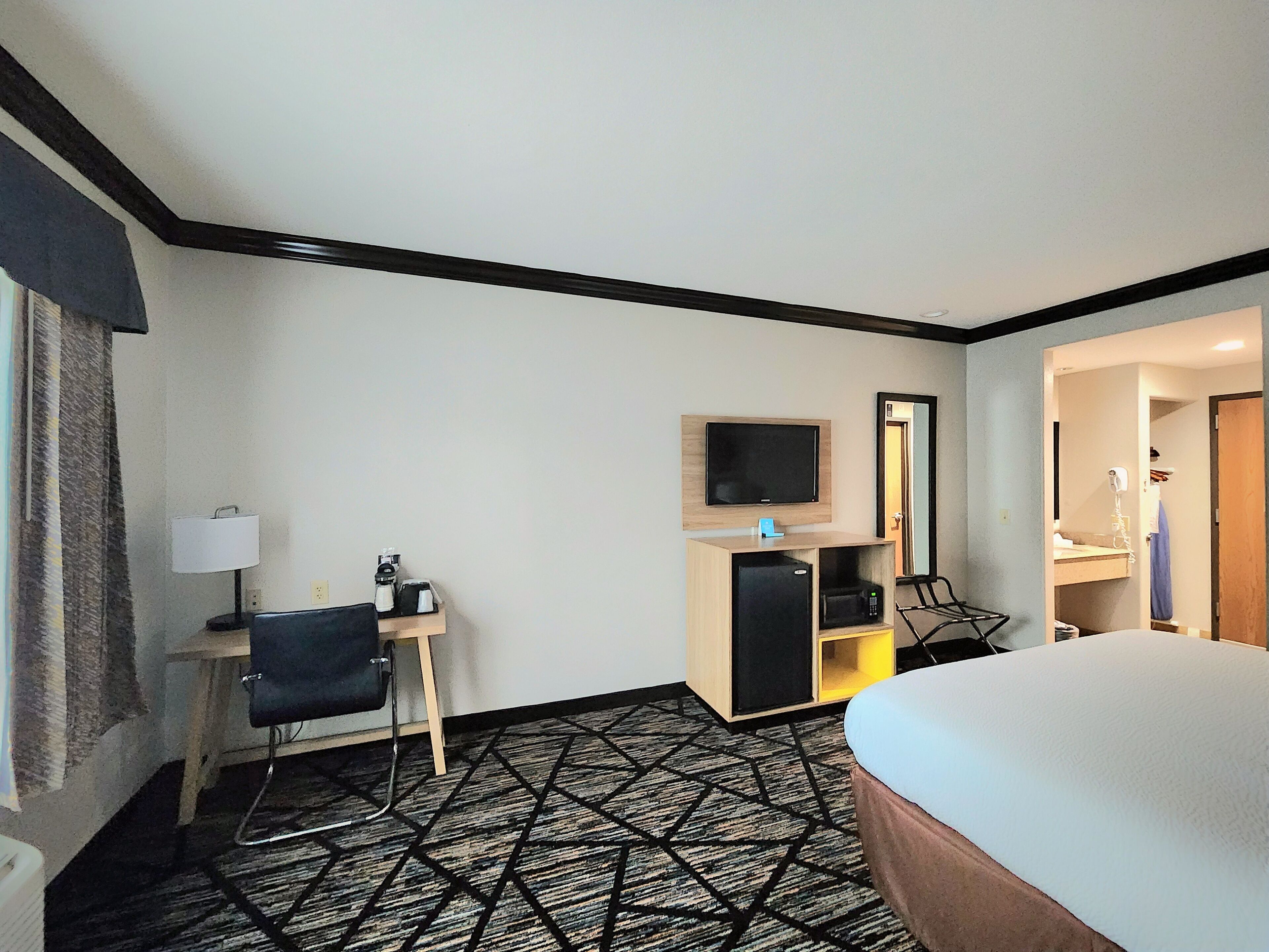 Ein Hotelzimmer mit einem Bett, einem Schreibtisch mit Stuhl, einem Fernseher, einer Mikrowelle und einem kleinen Kühlschrank.