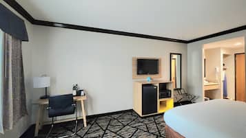 Ein Hotelzimmer mit einem Bett, einem Schreibtisch mit Stuhl, einem Fernseher, einer Mikrowelle und einem kleinen Kühlschrank.