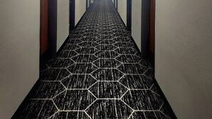 Pasillo de hotel con alfombra de estampado geométrico, puertas a ambos lados y lámparas fijadas a la pared.