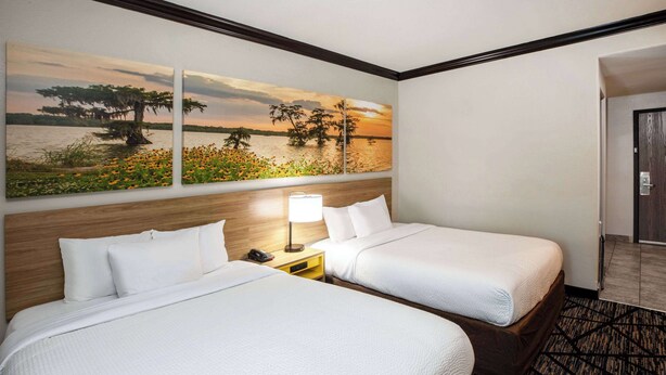 Habitación de hotel con dos camas, una mesita de noche con lámpara y un cuadro de un atardecer sobre el agua.