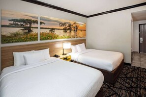 Habitación de hotel con dos camas, una mesita de noche con lámpara y un cuadro de un atardecer sobre el agua.