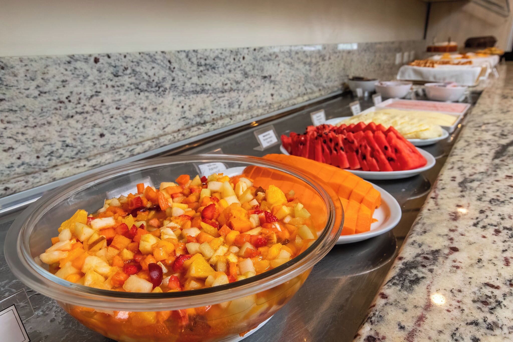 A buffet with various fruit options and a granite countertop.