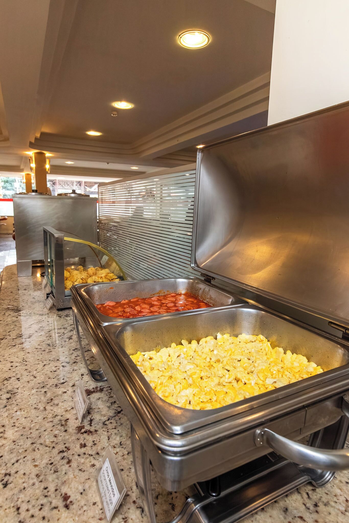 Zona de bufé con diversas opciones de comida, entre ellas huevos revueltos y un plato con salsa roja.