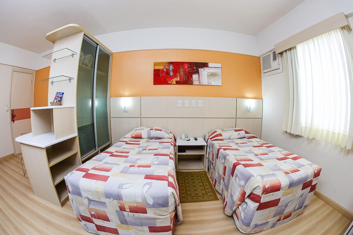 Une chambre d’hôtel avec deux lits, un bureau, une armoire et un tableau au mur.