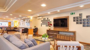 Een hotel lobby met een zithoek, een receptiebalie, een televisie en een muur met ingelijste foto's.