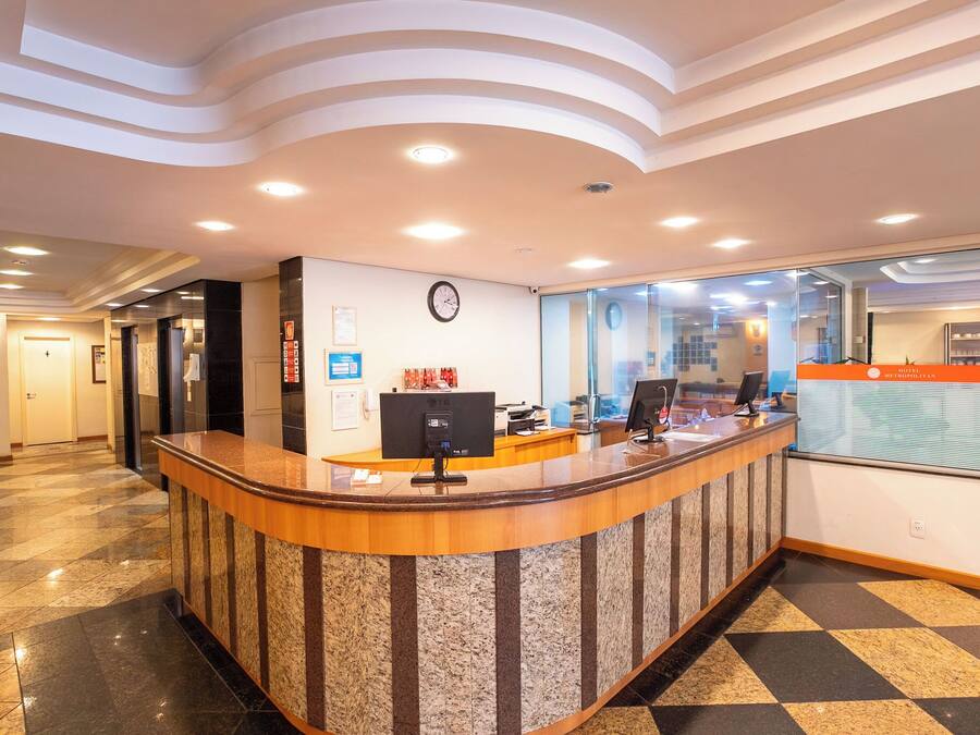 Zona de recepción de hotel con un mostrador curvo, un reloj en la pared y un separador de vidrio.
