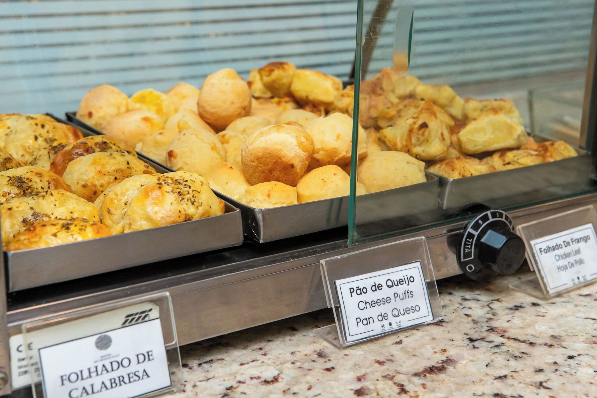 A buffet with various cheese and bread options, including 'Pão de Queijo' and 'Folhado de Calabresa'.