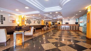 Een hotel lobby met een zwart-wit geruit vloerkleed, een zithoek, een receptiebalie en een modern plafondontwerp.