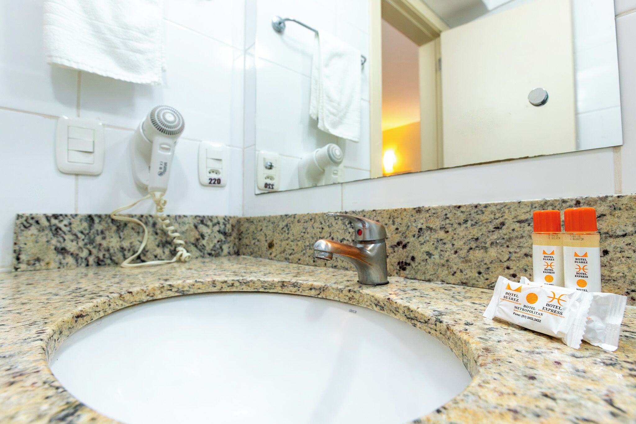 A bathroom with a granite countertop, a sink, a mirror, and toiletries.