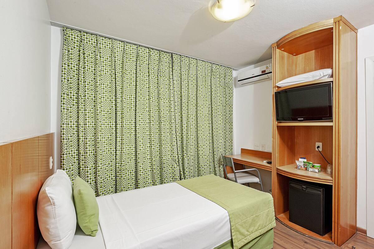 Ein kleines Hotelzimmer mit einem Bett, einem Schreibtisch, einer kleinen Kühlschrank und einem Fernseher.