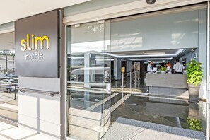 A hotel entrance with a reception desk, a glass door, and a sign reading "Slim Hotels".