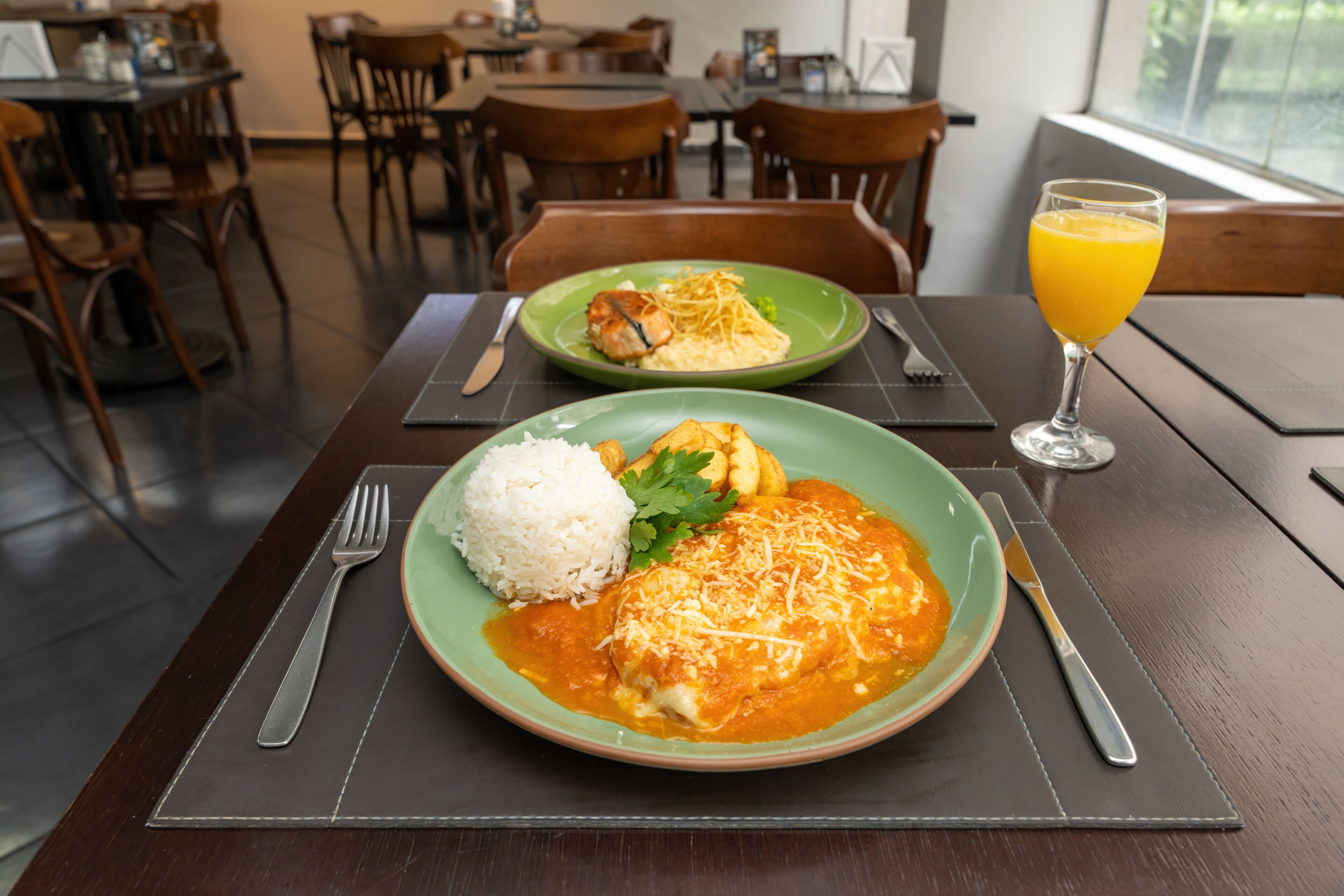A dining table with a plate of enchiladas, rice, and a glass of orange juice.