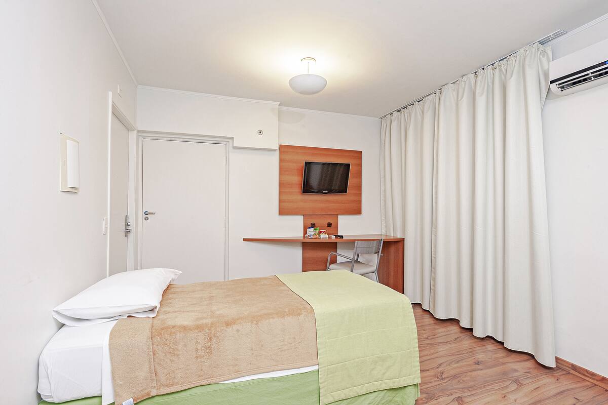 Ein Hotelzimmer mit einem Bett, einem Schreibtisch, einem Stuhl, einem Fernseher und einem Vorhang.