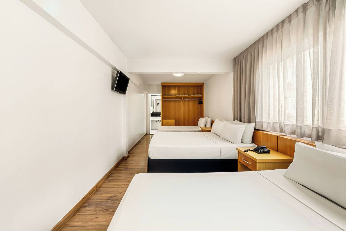 Ein Hotelzimmer mit zwei Betten, einem Holzschrank, einem Nachttisch mit Lampe und einem an der Wand befestigten Fernseher.