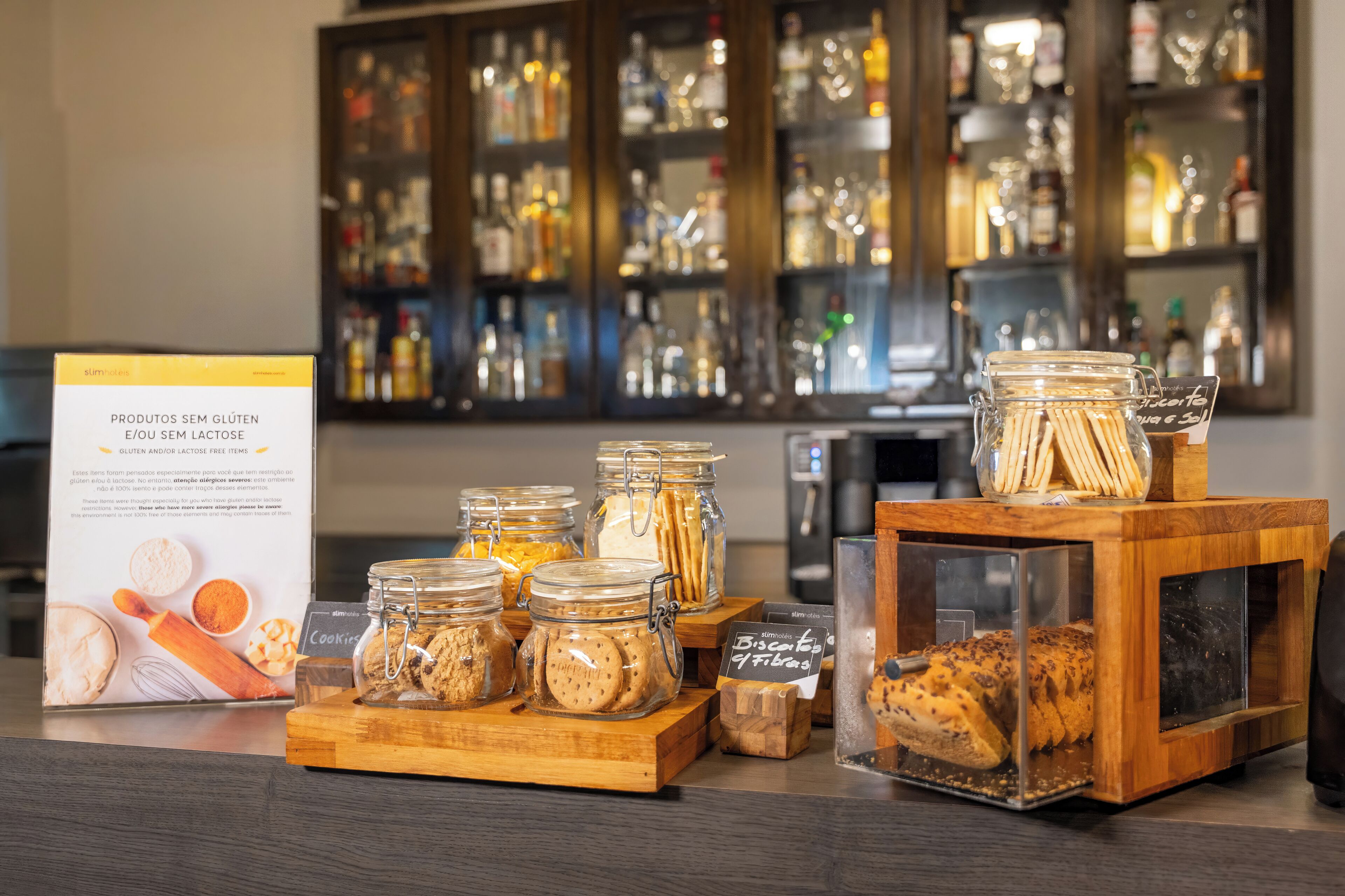 A display of gluten-free and lactose-free products, including cookies and bread, in a store with a background of shelves stocked with various bottles.