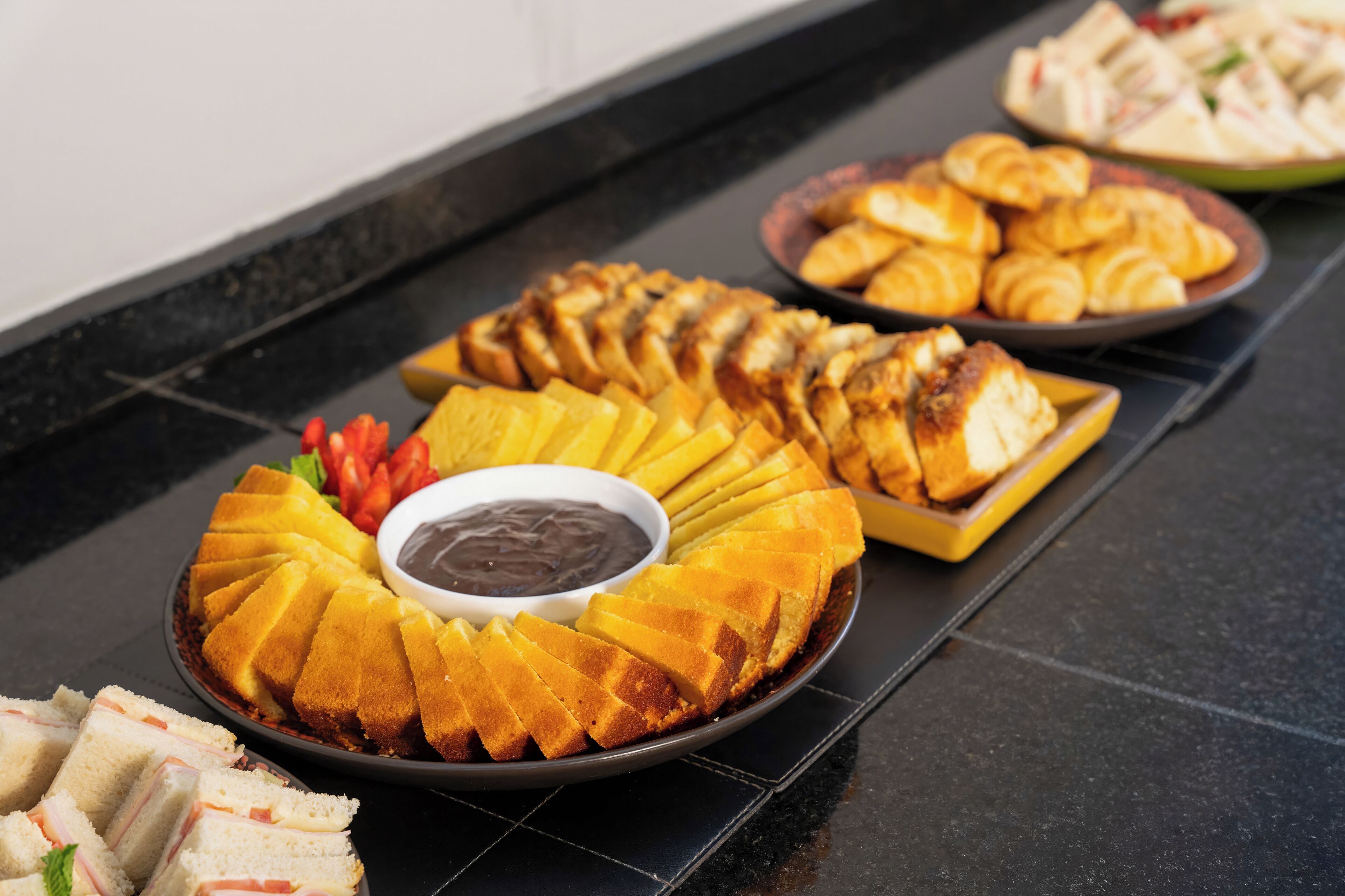 Une table de buffet proposant divers plats, notamment des tranches d’ananas, des sandwichs et des pâtisseries.