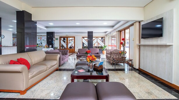 A spacious lobby with a sofa, armchairs, a coffee table, and a TV mounted on the wall. - Hotel Suárez Campo Bom (Campo Bom)