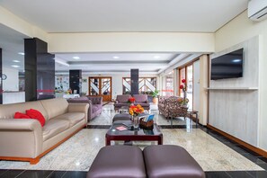 A spacious lobby with a sofa, armchairs, a coffee table, and a TV mounted on the wall. - Hotel Suárez Campo Bom (Campo Bom)