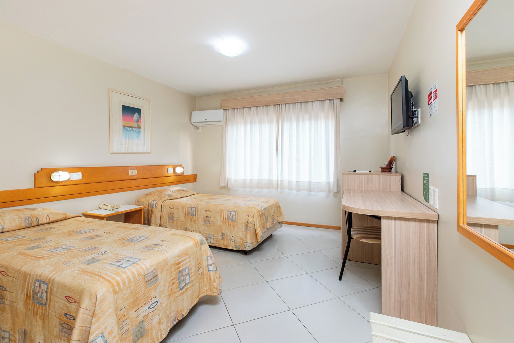 Una camera d'hotel con due letti, una scrivania, una televisione e una finestra con tende.