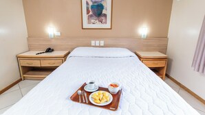 A hotel room with a bed, two bedside tables, a tray with food, a painting on the wall, and an air conditioning unit. - Hotel Suárez Campo Bom (Campo Bom)
