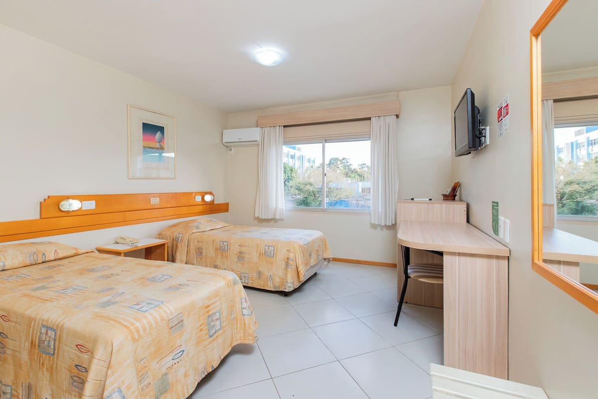 A hotel room with two beds, a desk, a TV, and a window with curtains.