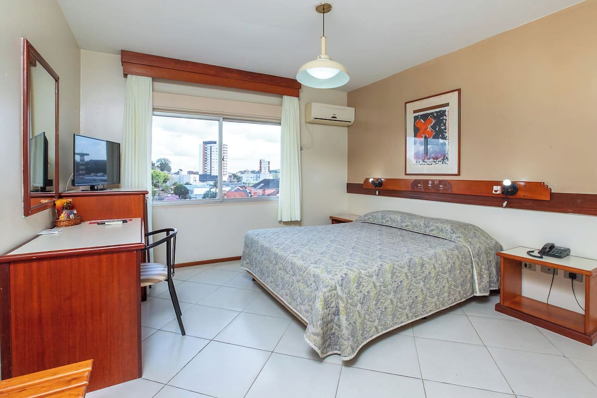 A hotel room with a bed, desk, chair, and a TV.