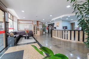 A hotel lobby with a reception desk, a sofa, a coffee table, and a potted plant.