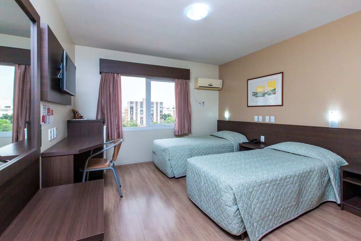 Ein Hotelzimmer mit zwei Betten, einem Schreibtisch, einem Stuhl, einem Fernseher und einem fenster mit Vorhängen.