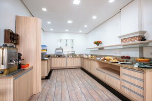 A modern kitchen with wooden cabinets, a stainless steel coffee machine, and a variety of food items on the counter.